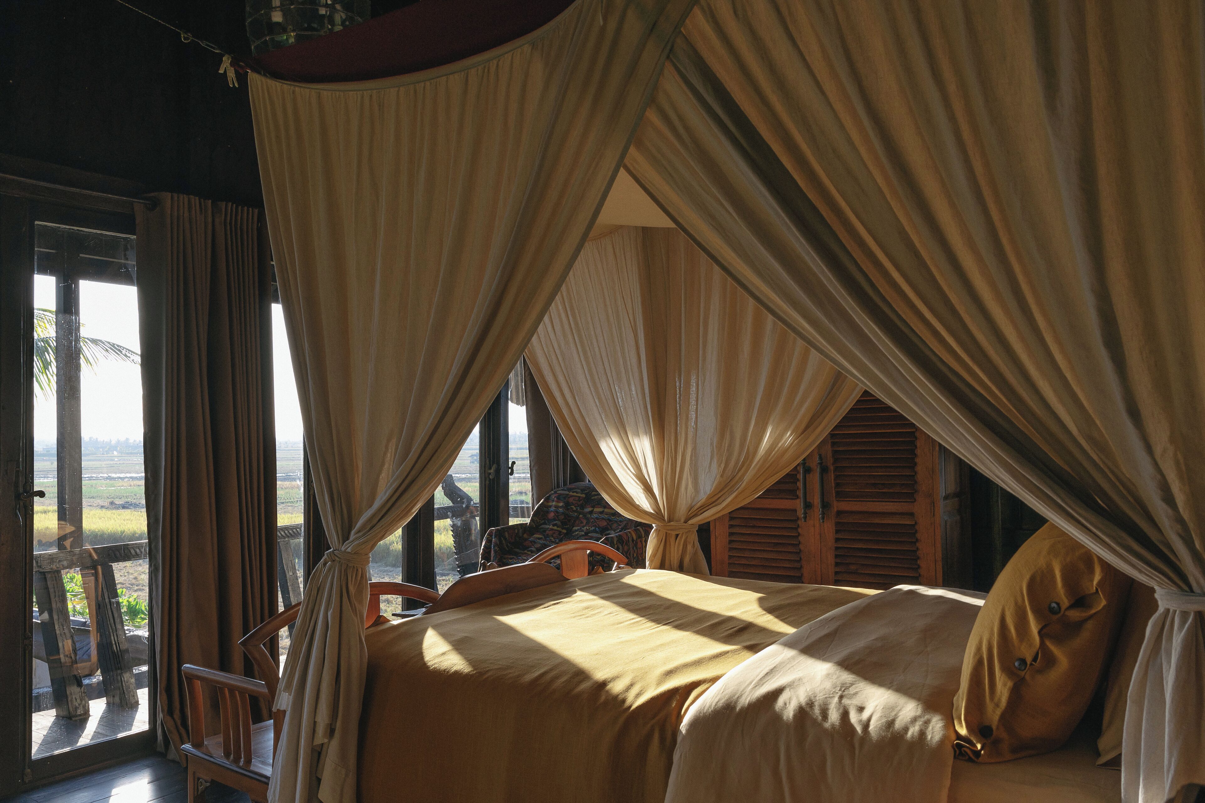 A room with a bed, curtains, and a view through a window.