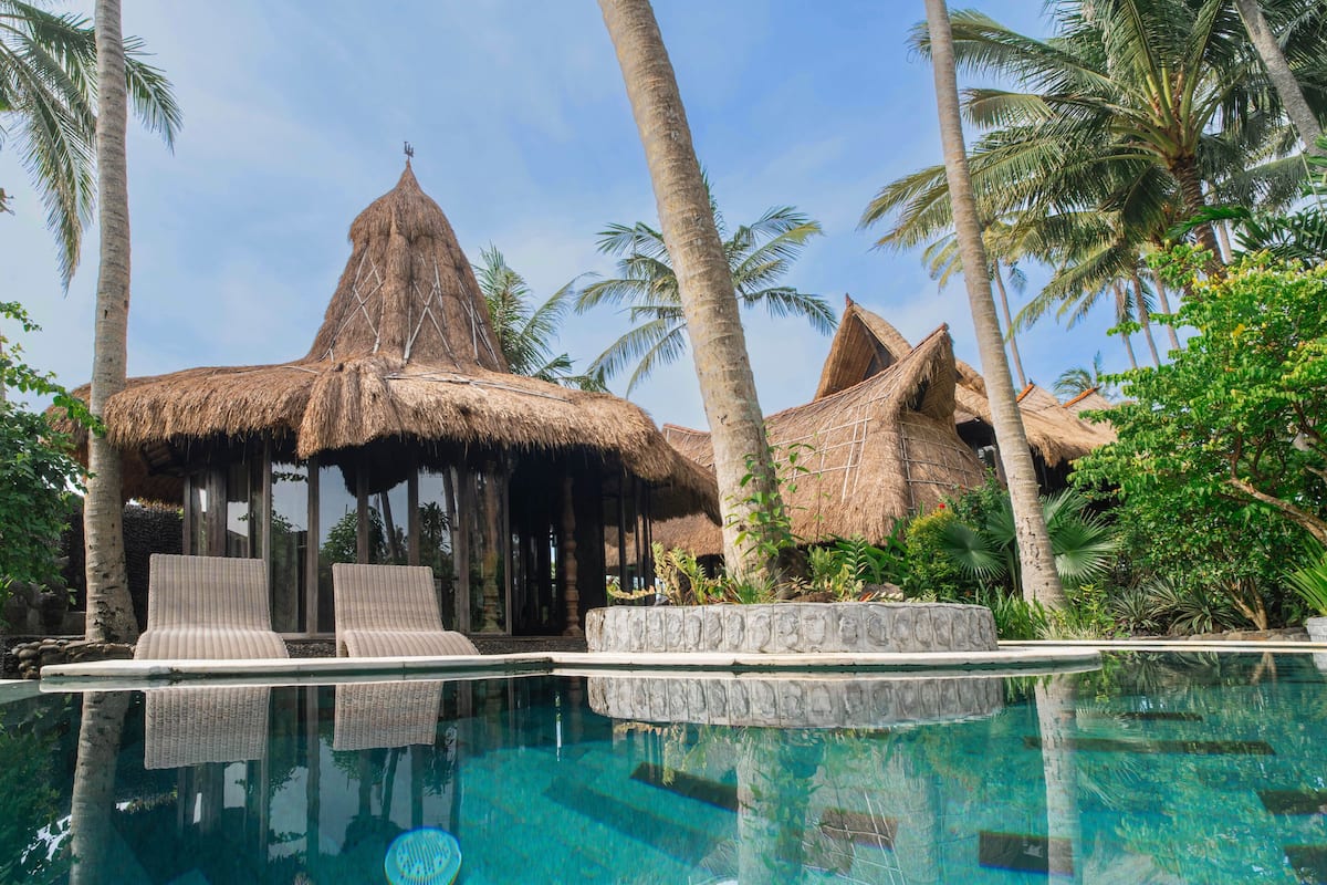 A pool area with lounge chairs, thatched-roof structures, and palm trees.