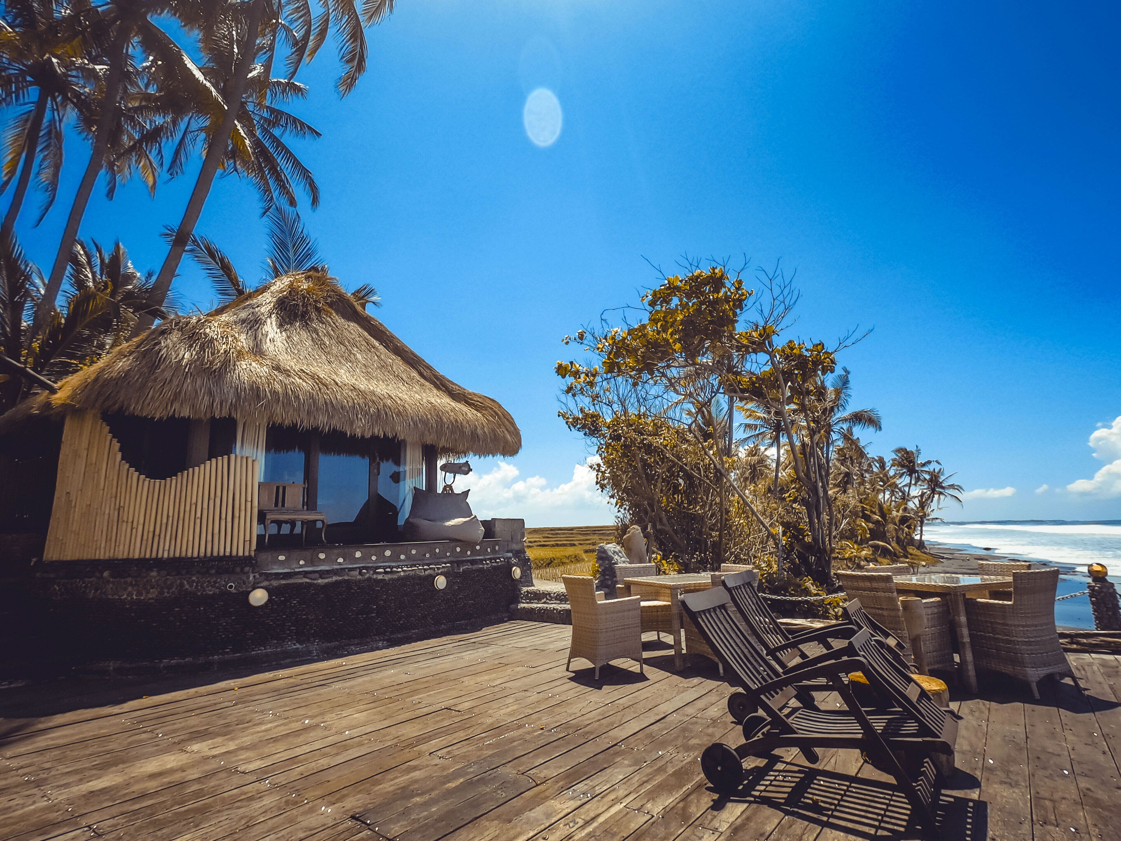 A wooden deck with lounge chairs, a thatched-roof hut, and a view of the ocean.