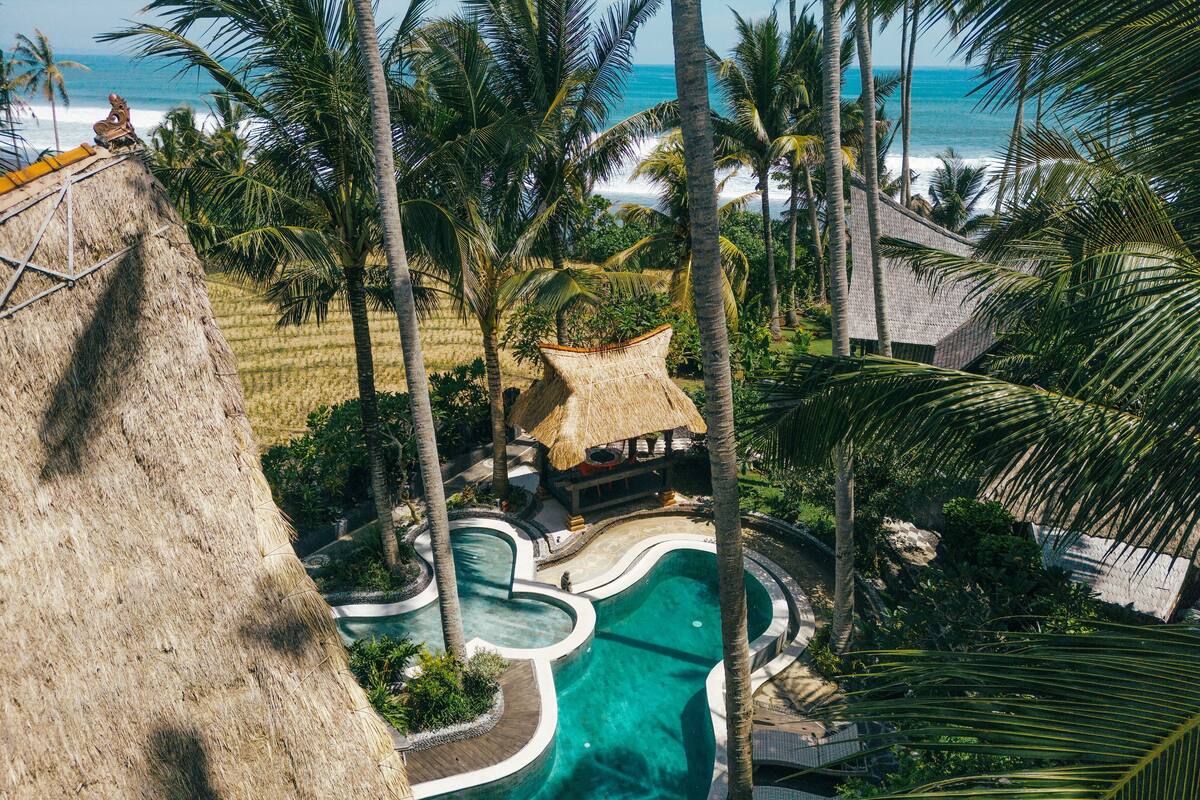 A resort with a pool, palm trees, and a view of the ocean.