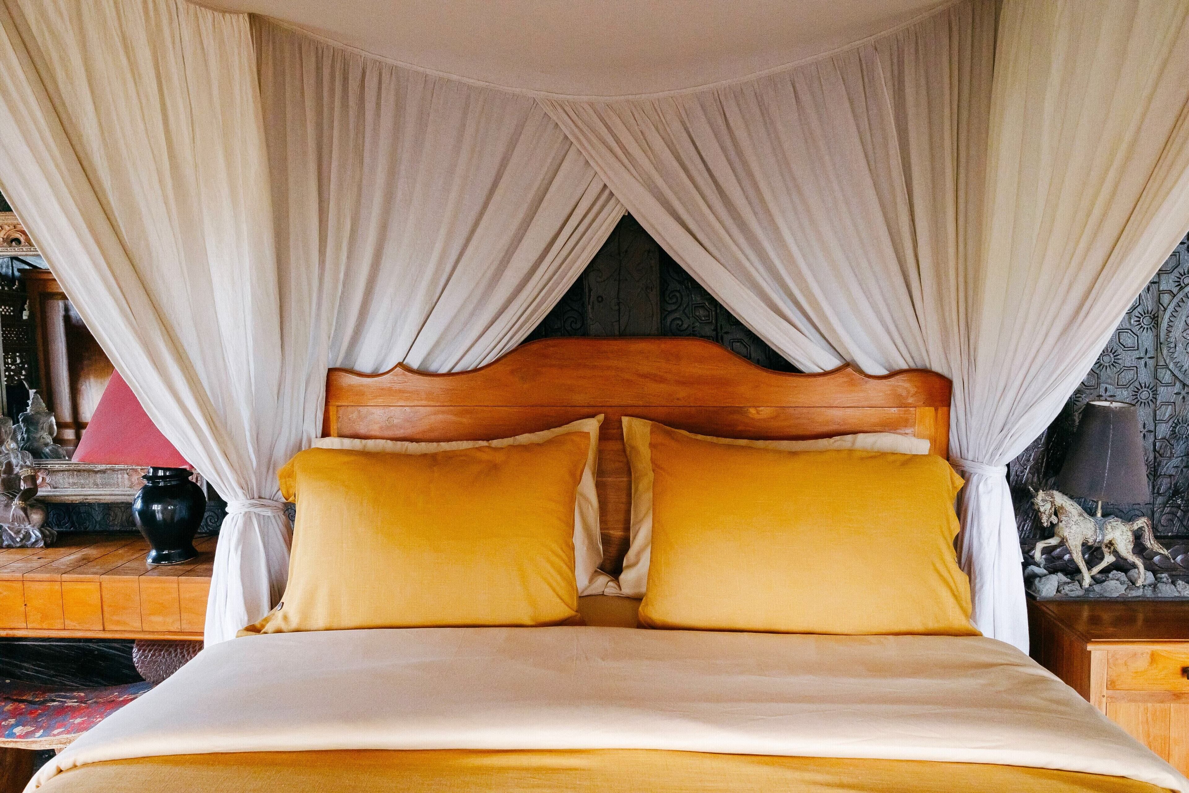 A bed with a wooden headboard, white curtains, and two yellow pillows.