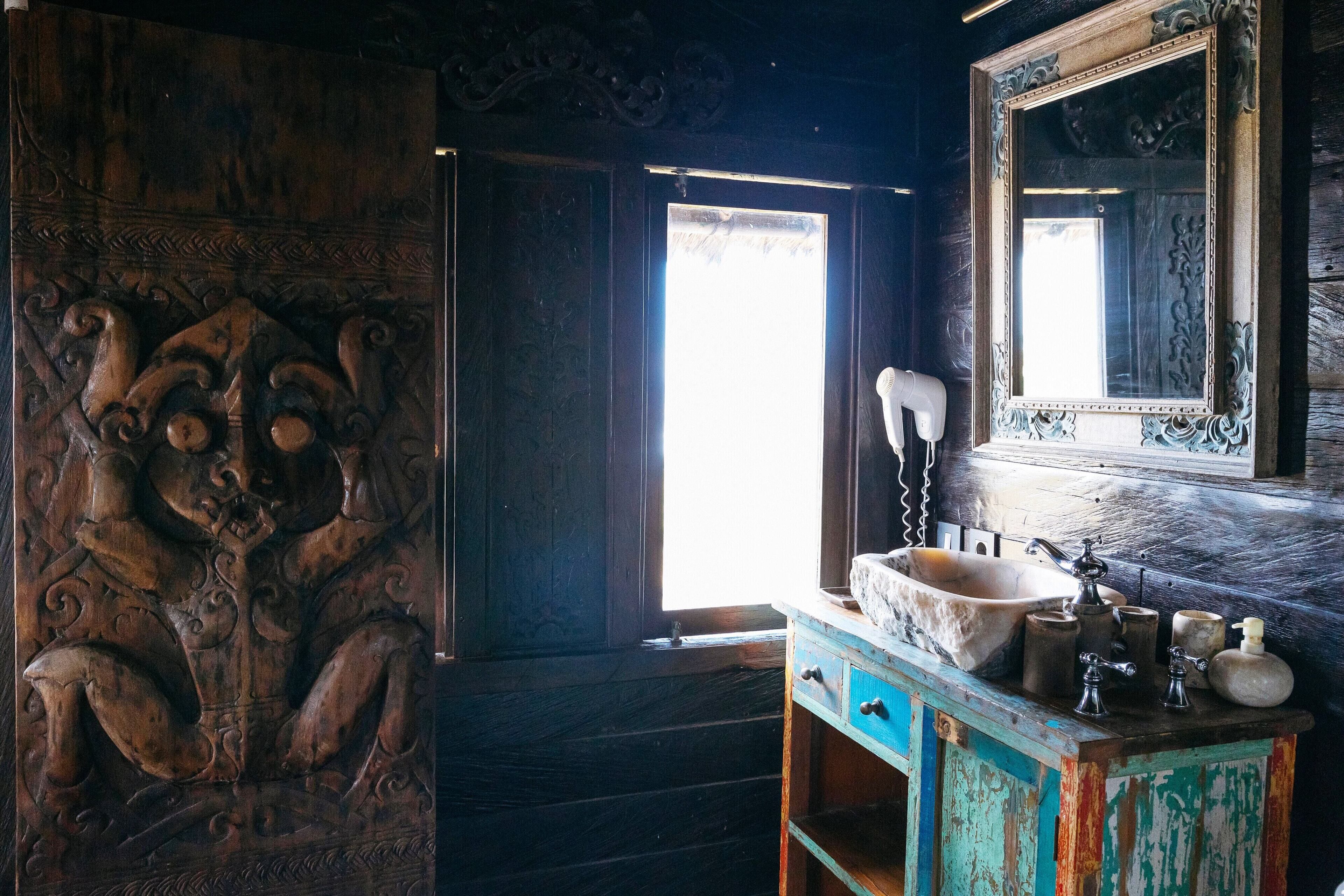 Un baño rústico con una puerta de madera, un espejo grande y un lavamanos antiguo.