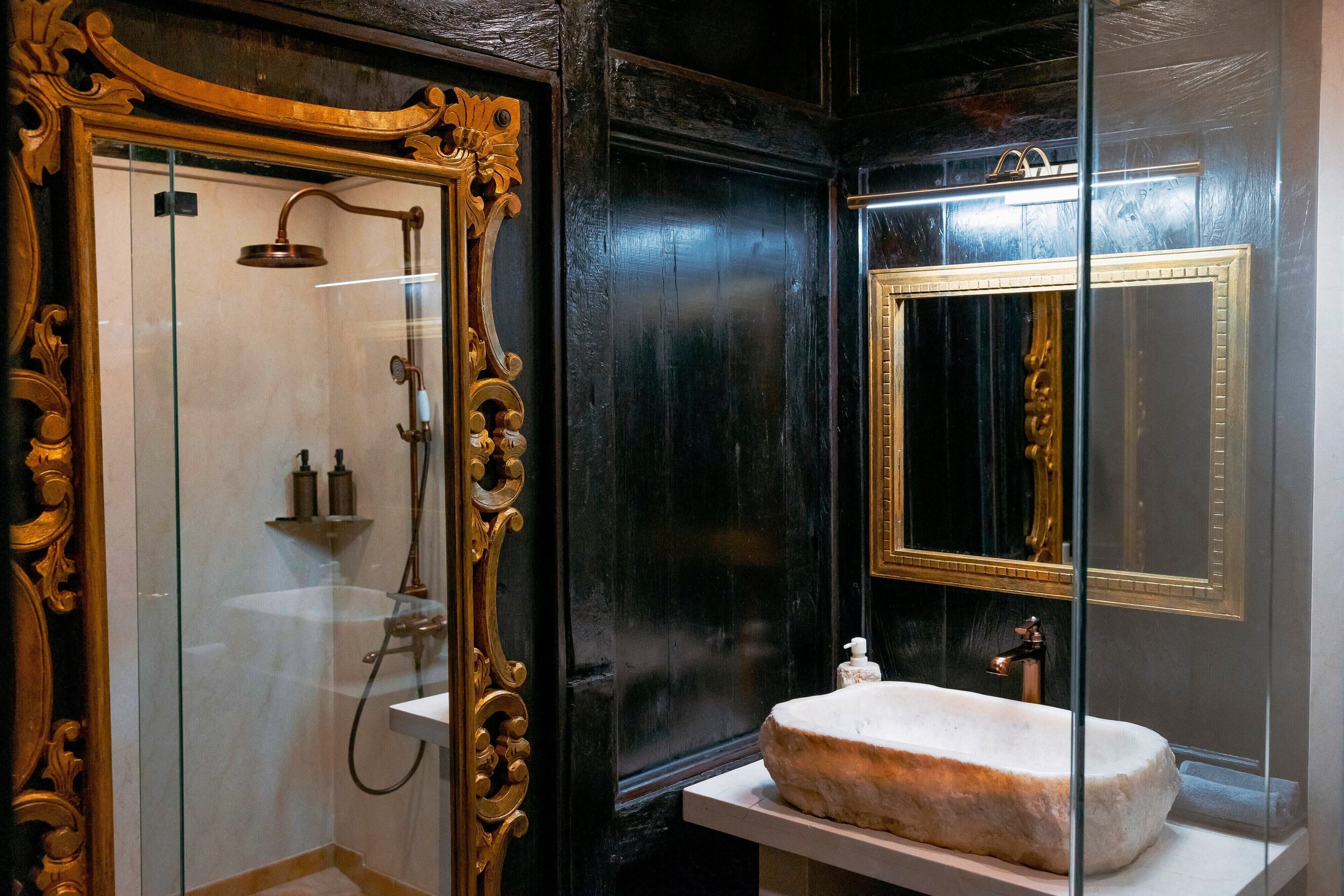 A bathroom with a glass-enclosed shower, a marble sink, and ornate gold-framed mirrors.
