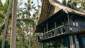 A traditional wooden house with a thatched roof, surrounded by tall palm trees. - Most Exotic Beachfront Villa Keong (Tabanan)