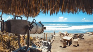 A beachside patio with wicker furniture, a metal grill, and a thatched roof. - Most Exotic Beachfront Villa Keong (Tabanan)
