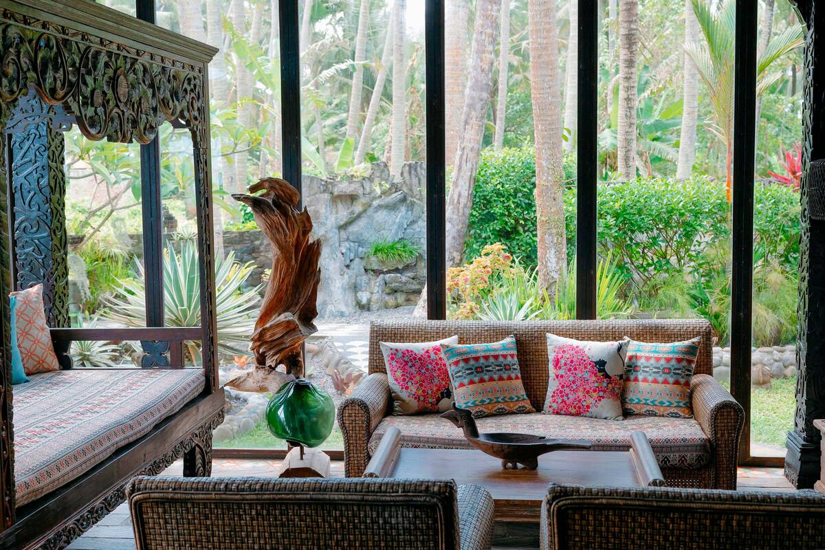 A room with a sofa set, a decorative bird sculpture, and a view of a tropical garden through large windows.