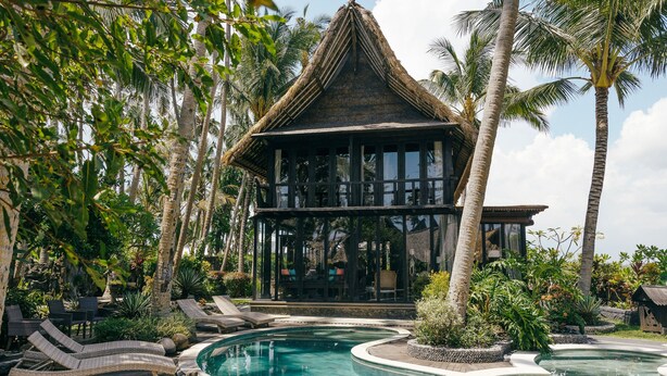 A pool area with lounge chairs and a thatched-roof building. - Most Exotic Beachfront Villa Keong (Tabanan)