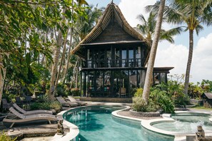 A pool area with lounge chairs and a thatched-roof building. - Most Exotic Beachfront Villa Keong (Tabanan)