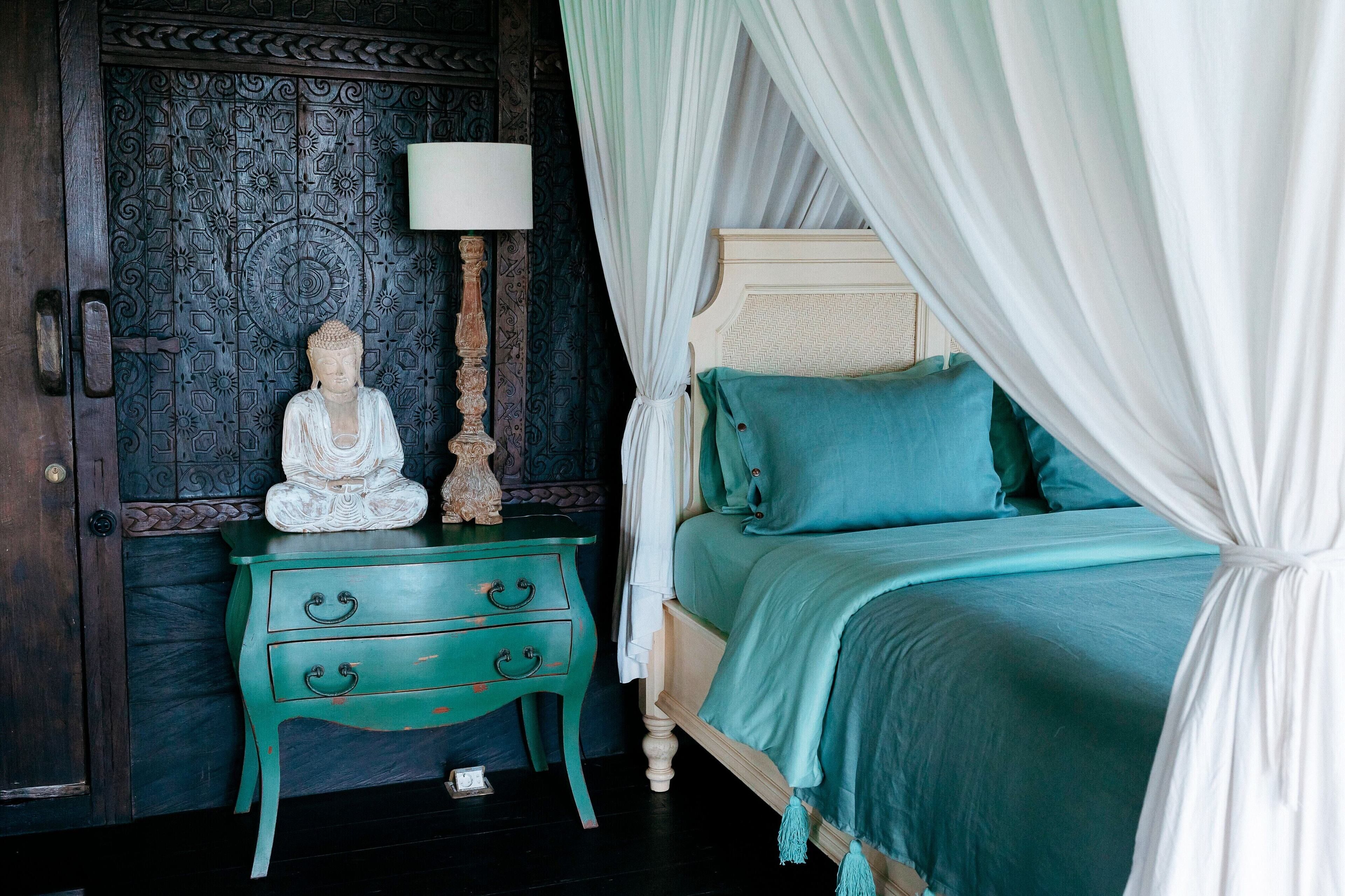 A room with a bed, a nightstand, a Buddha statue, and a decorative door.