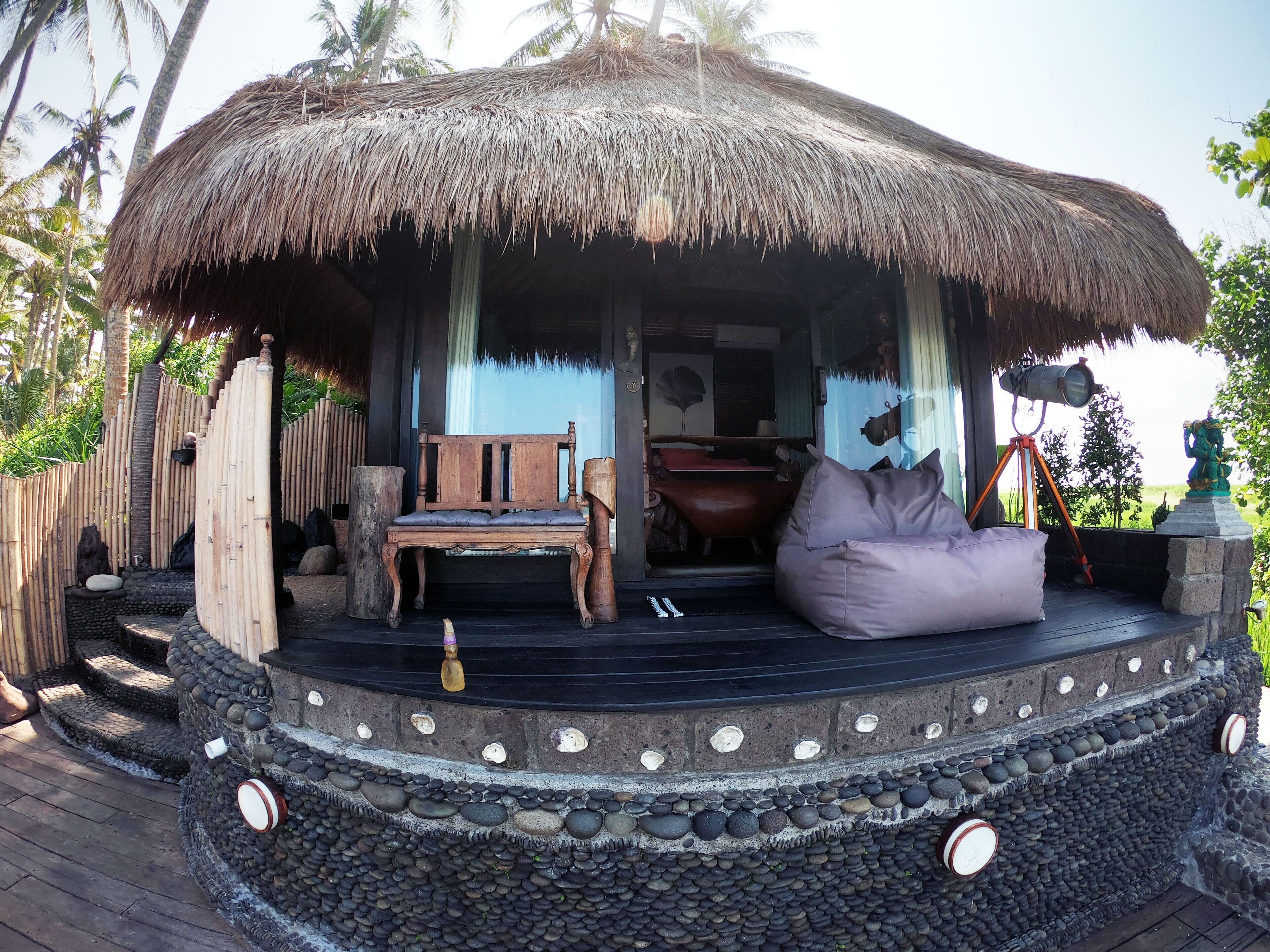 A thatched-roof structure with a wooden bench and a bean bag chair, surrounded by a stone wall with decorative elements.