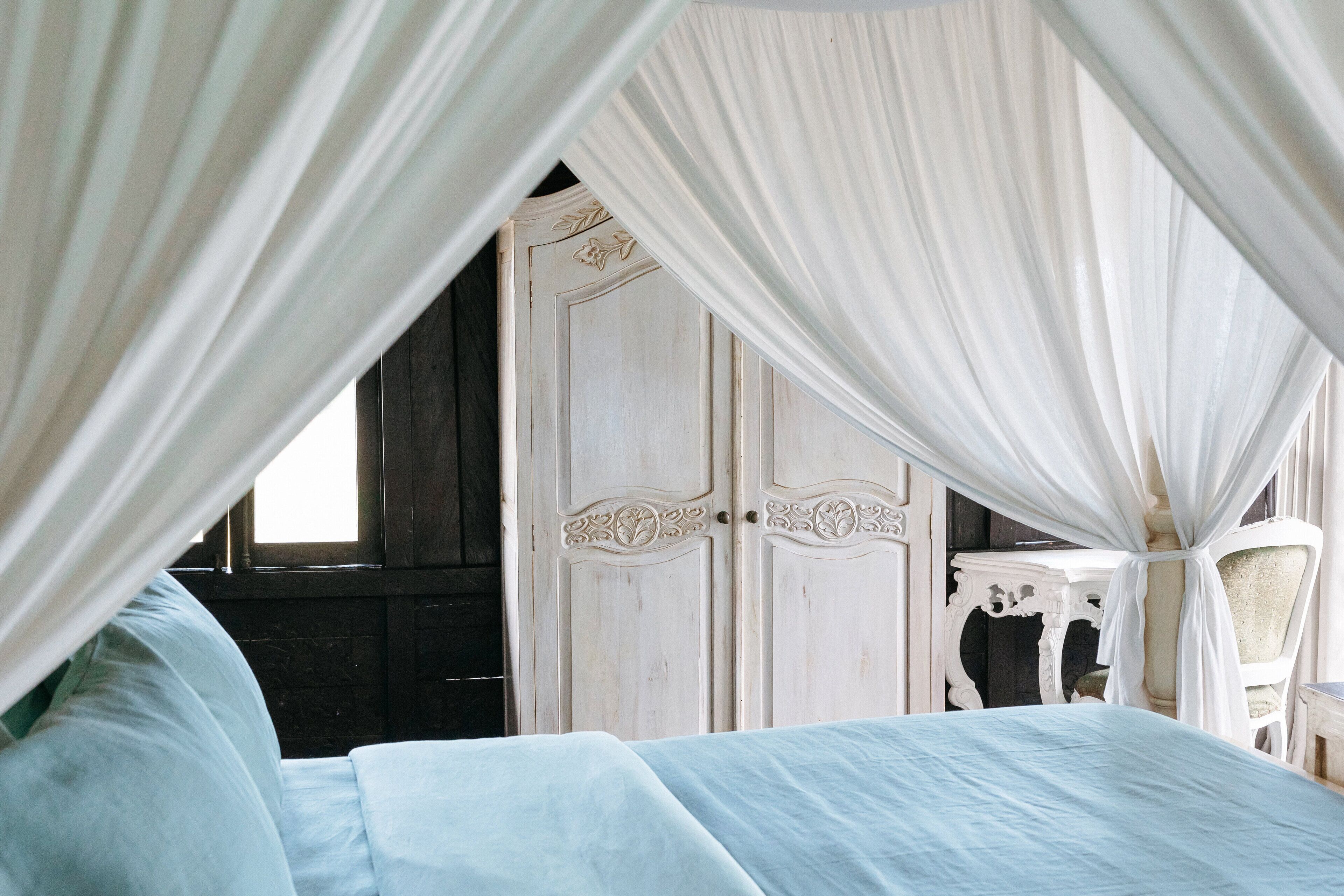 A bedroom with a canopy bed, a wardrobe, and a chair.