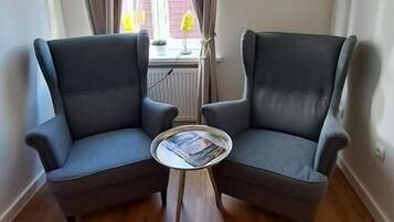 Une pièce comprenant deux fauteuils, une petite table ronde et une fenêtre avec des rideaux.