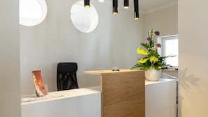 En receptionsdisk med træpanel, en potteplante med gule og lilla blomster, og en sort stol.