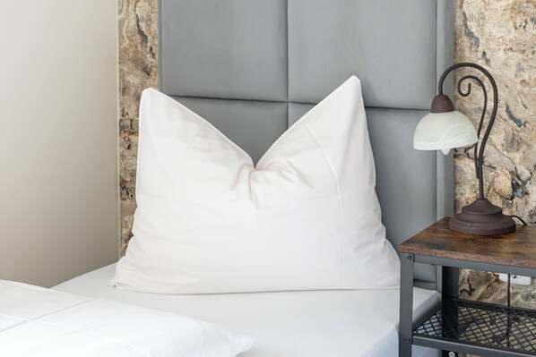 A bed with a white pillow, a bedside table with a lamp, and a textured wall behind.