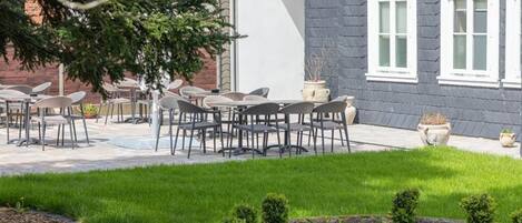 An outdoor seating area with tables and chairs, a well-maintained lawn, and a building with windows.
