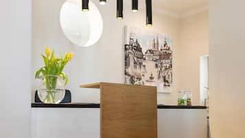 Un mostrador de recepción con paneles de madera, un jarrón de cristal con flores amarillas, un espejo redondo y una lámpara colgante negra.