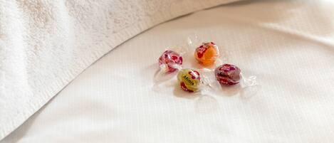 Un lit avec un drap blanc et quatre bonbons emballés posés dessus.