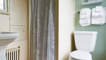 A bathroom with a toilet, a radiator, a shower curtain, and a towel rack.