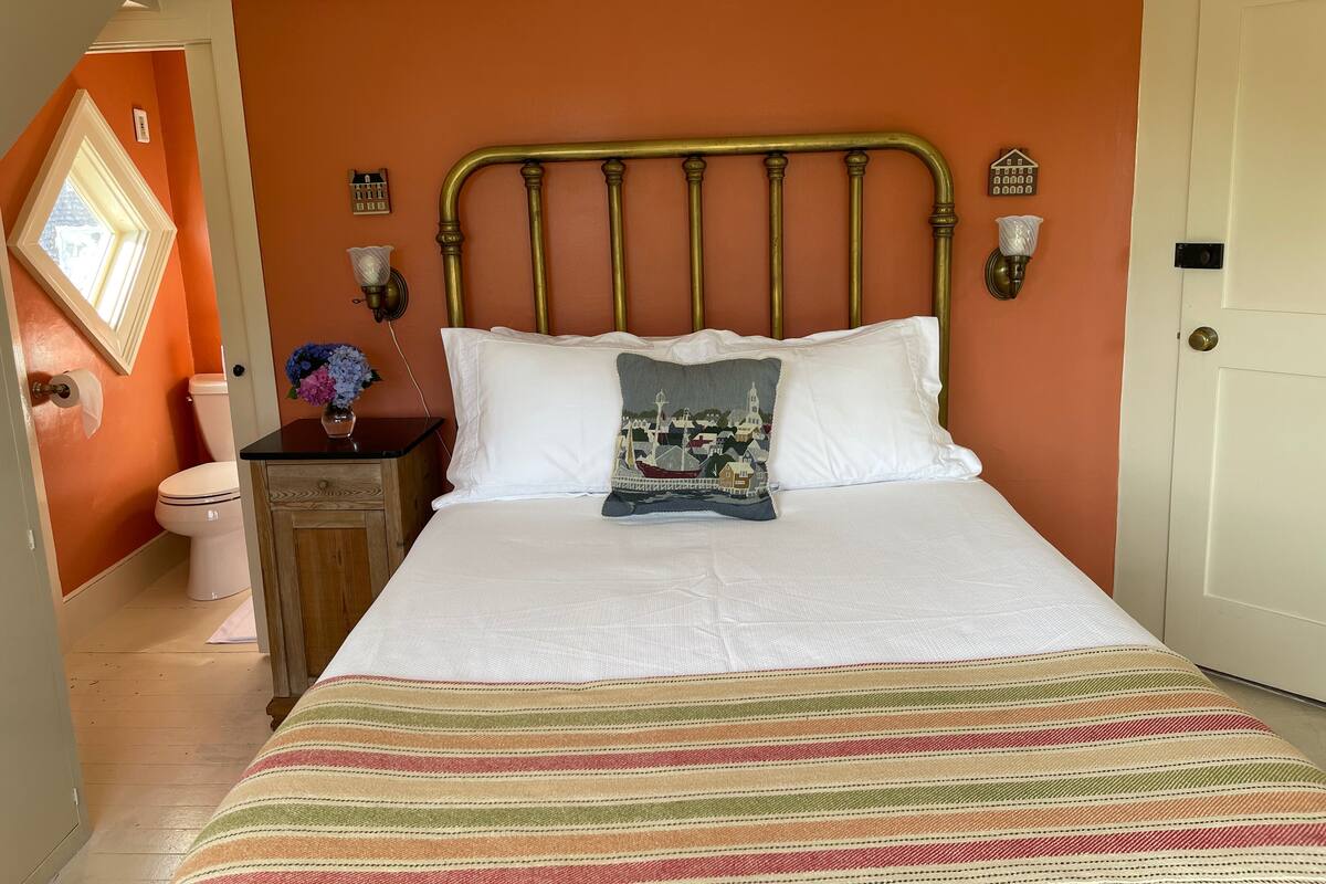A bedroom with a bed, a nightstand, a wall-mounted lamp, and a window.