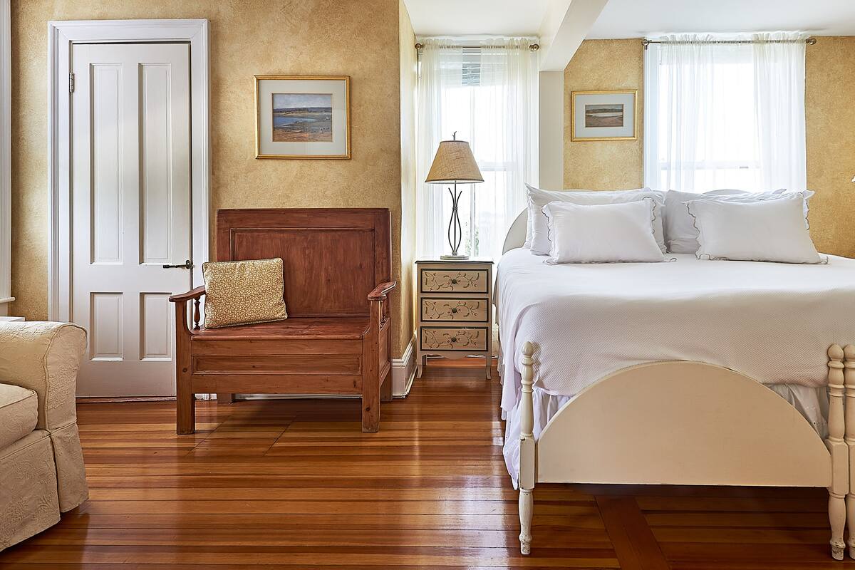 A bedroom with a wooden bed, a wooden chair, a nightstand, and a door.
