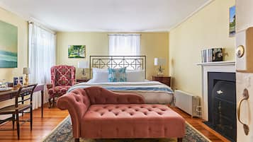 A bedroom with a large bed, a sitting area with a chair, a desk, and a fireplace.