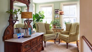 A cozy living room with a wooden dresser, two houndstooth armchairs, a side table with a lamp, and a large mirror. - Cliff Lodge (Nantucket)
