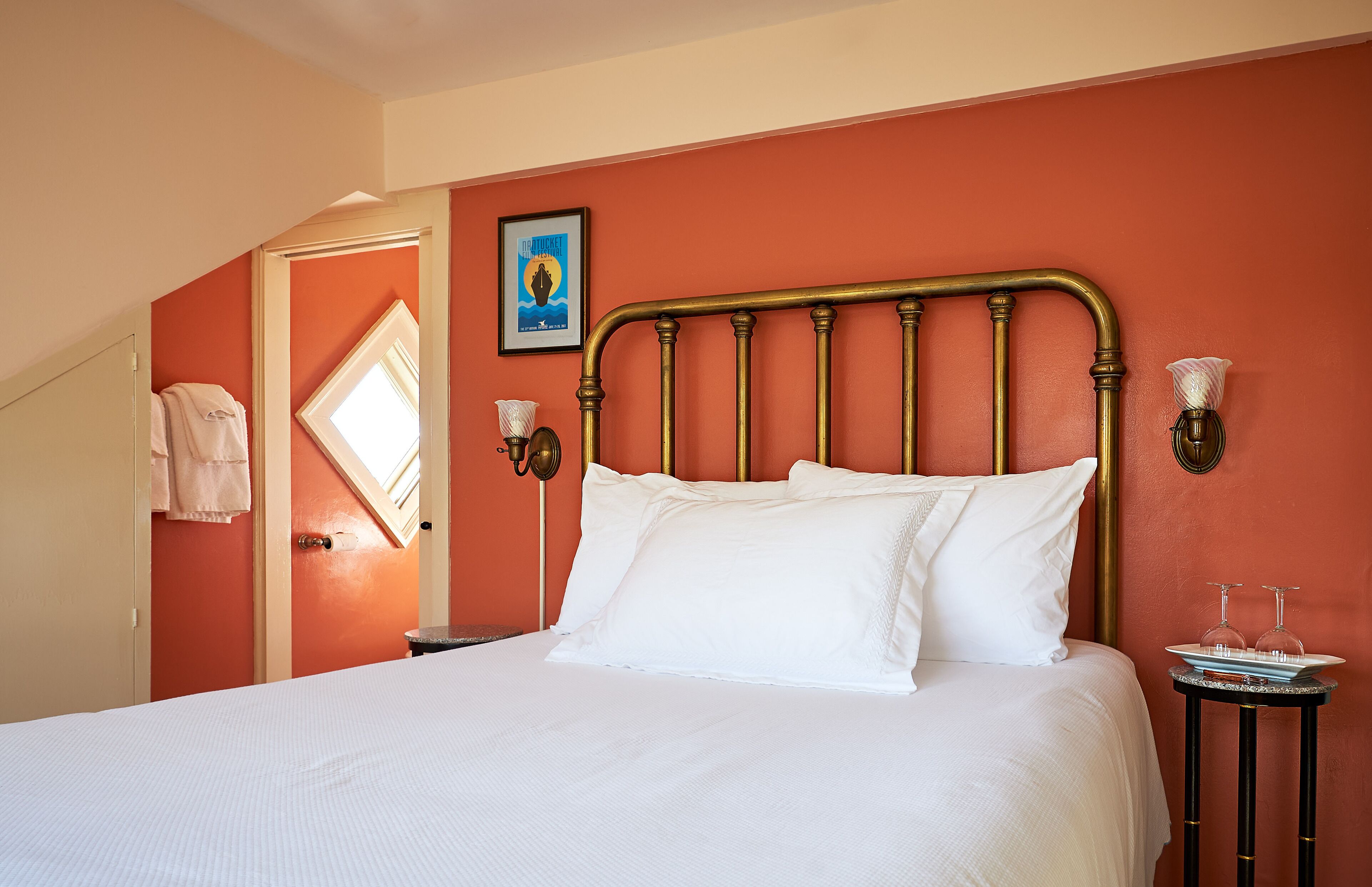 A neatly made bed with white linens, a brass headboard, and a small bedside table with a glass and a plate.