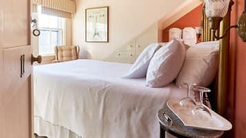 A neatly made bed with white linens, a bedside table with a tray holding wine glasses, and a framed picture of the Eiffel Tower on the wall.