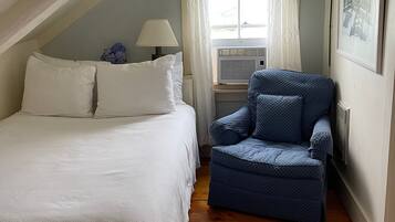 Un dormitorio con cama, una silla, una ventana con cortinas, una lámpara y un radiador.