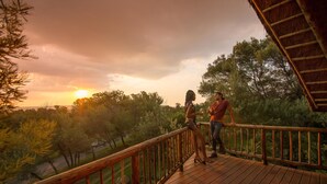 A wooden deck with a railing overlooking a scenic landscape during sunset.