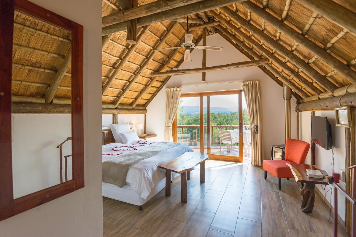 A bedroom with a bed, a wooden bench, a TV, and a balcony with a view.