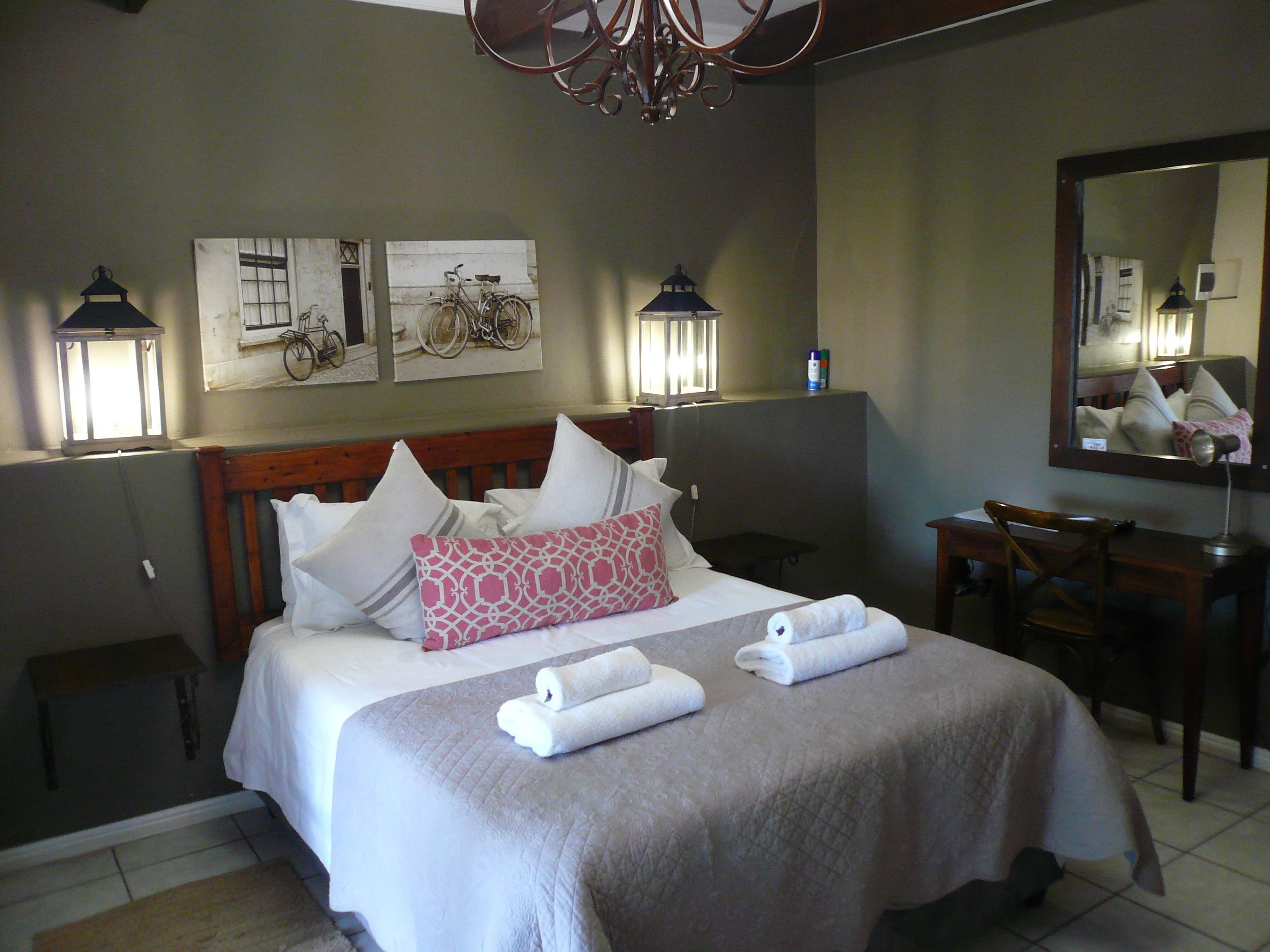 Uma cama bem arrumada com almofadas, mesa de cabeceira, cadeira e luminárias fixadas na parede.