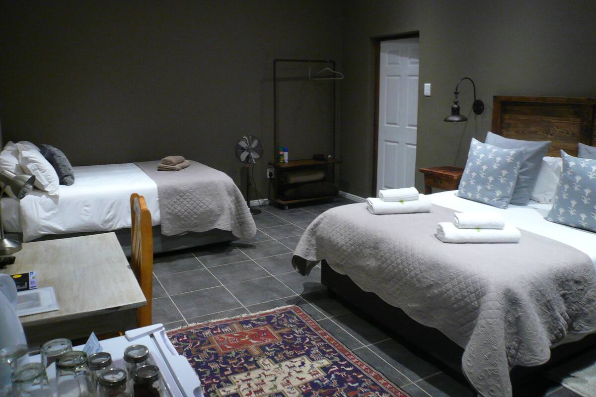 Ein Hotelzimmer mit zwei Betten, einem kleinen Tisch, einem Stuhl, einem Ventilator und einem Teppich.
