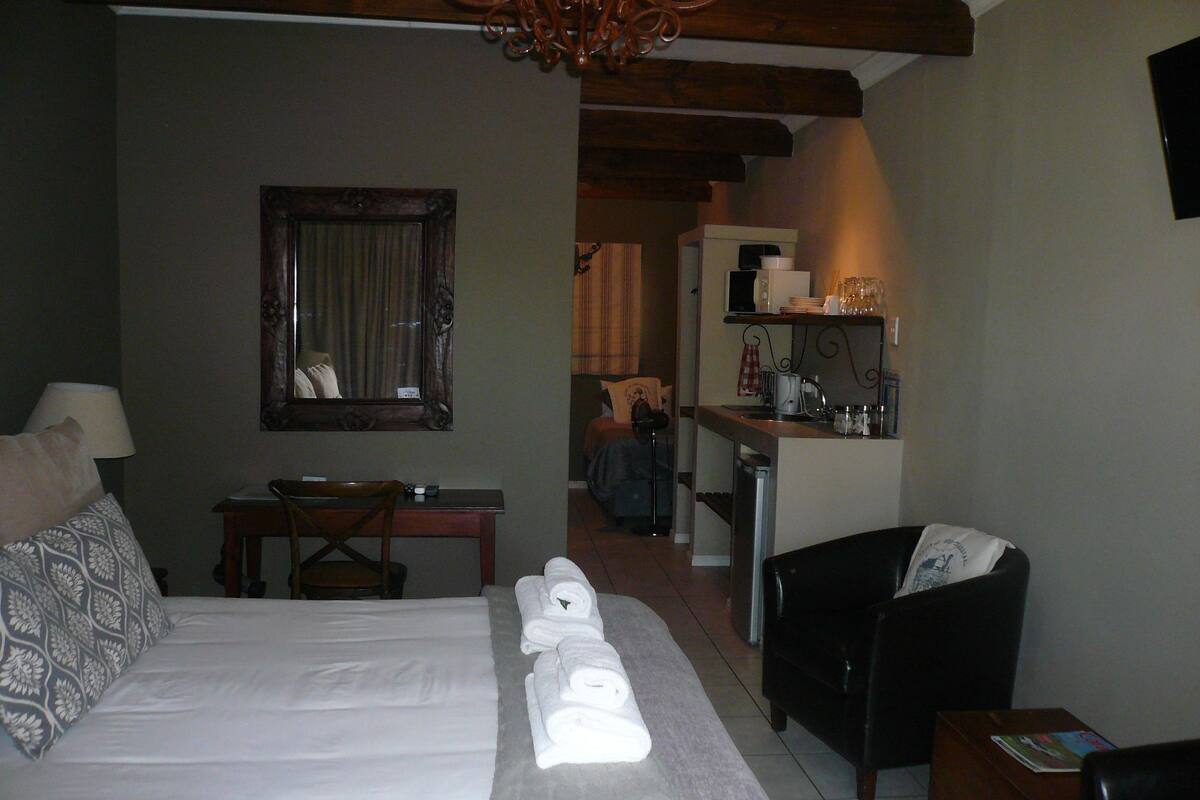 Ein Hotelzimmer mit Bett, Schreibtisch, Stuhl, einer kleinen Küchenzeile und einem Fernseher.
