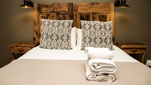 A neatly made bed with patterned pillows, a folded towel, and two bedside tables with lamps.