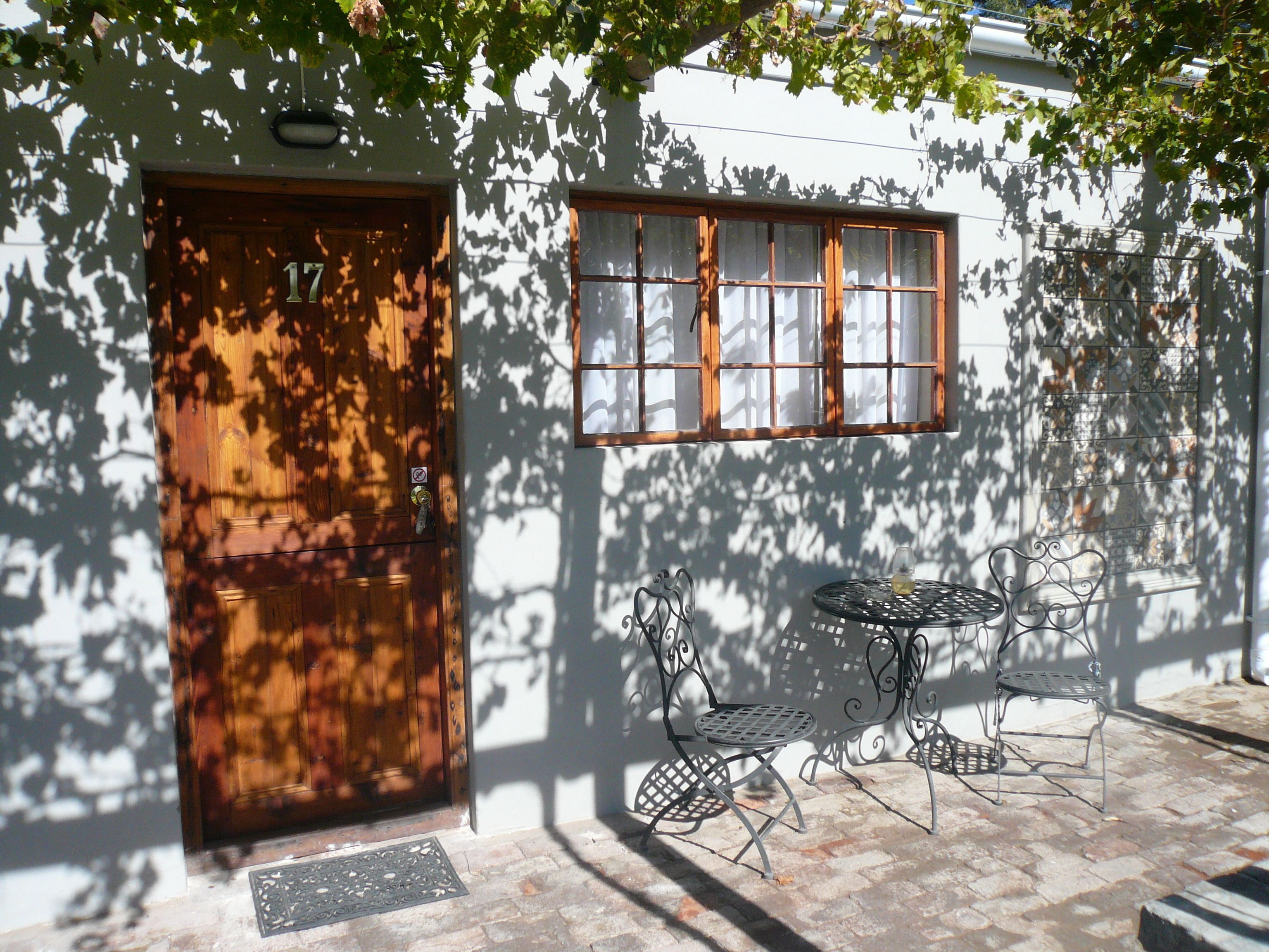 A wooden door with a number, a window with a grid pattern, and two metal chairs with a table.