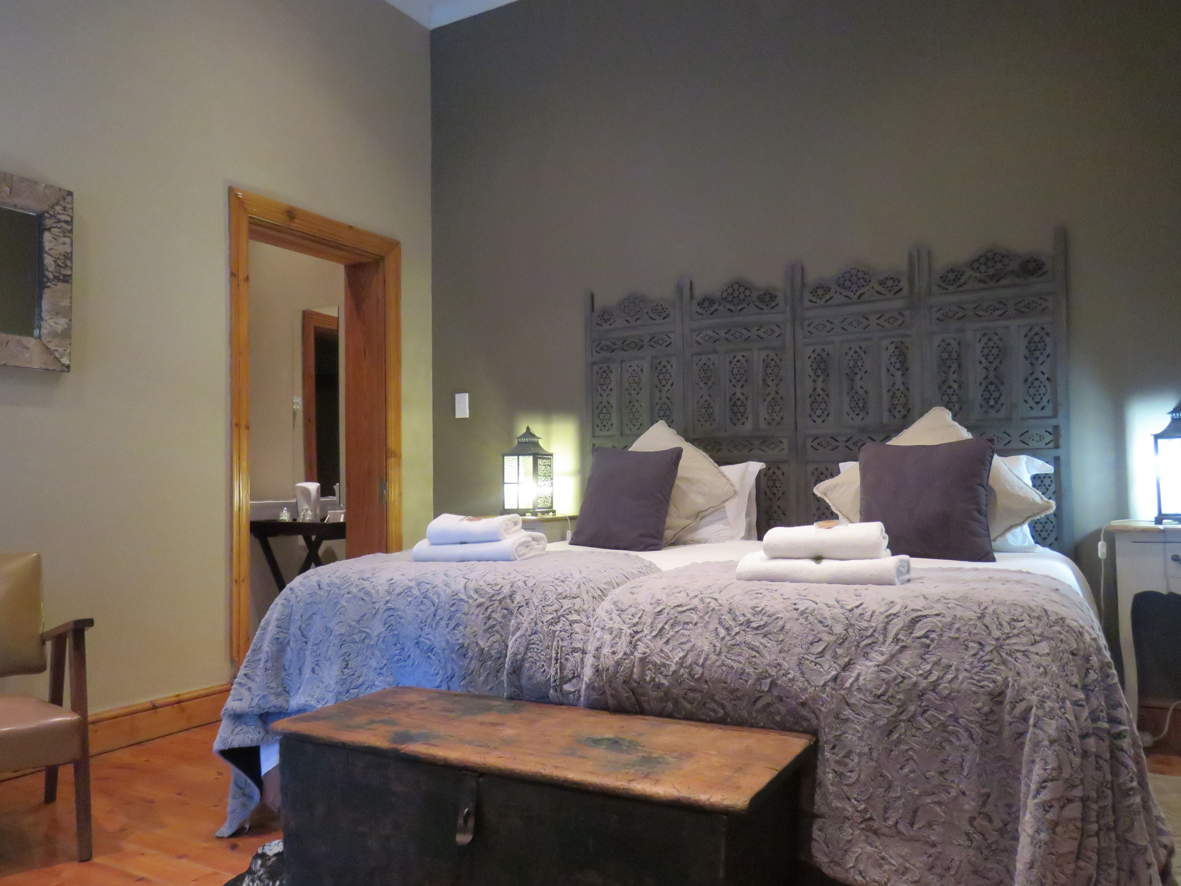 A hotel room with a large bed, two bedside tables, a bench, a mirror, and a decorative wall panel.