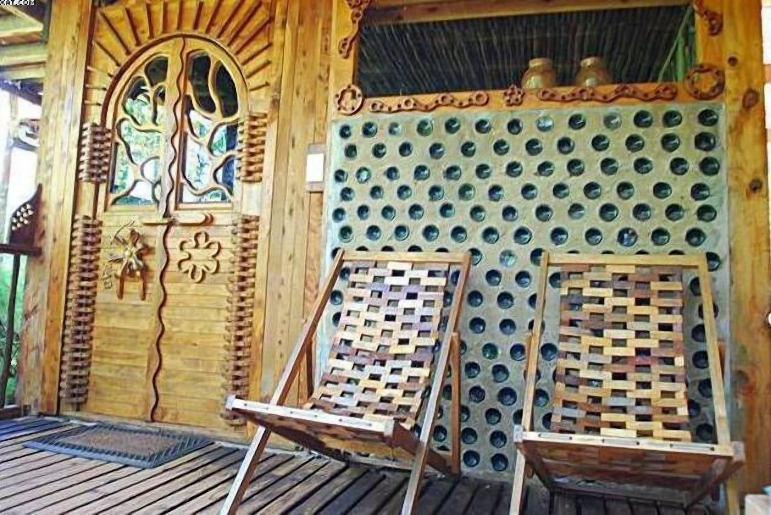 A wooden structure with a decorative door, a wall with circular holes, and two wooden chairs.