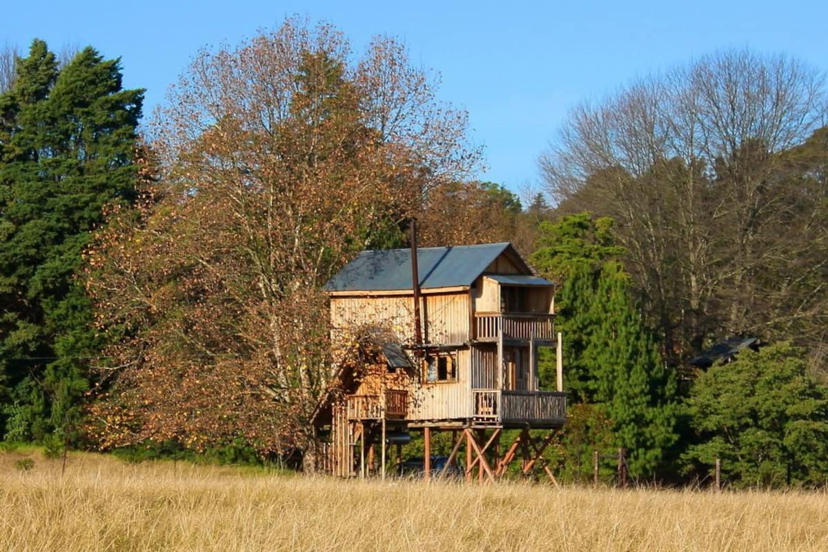 Une cabane en bois dotée d’un balcon, entourée d’arbres et d’un champ.