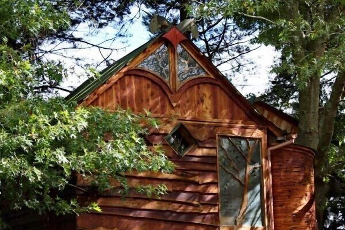 Une cabane rustique avec un toit en pente, une grande fenêtre et une cabane dans les arbres attenante à la structure principale.