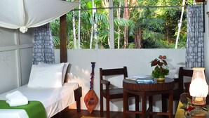 Una habitación con cama, una mesa con lámpara, una silla y vistas a la vegetación exuberante.