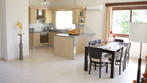 A modern kitchen with a central island, wooden cabinets, and a dining area with a table and chairs. - Vineland Holiday Villas (Pissouri)