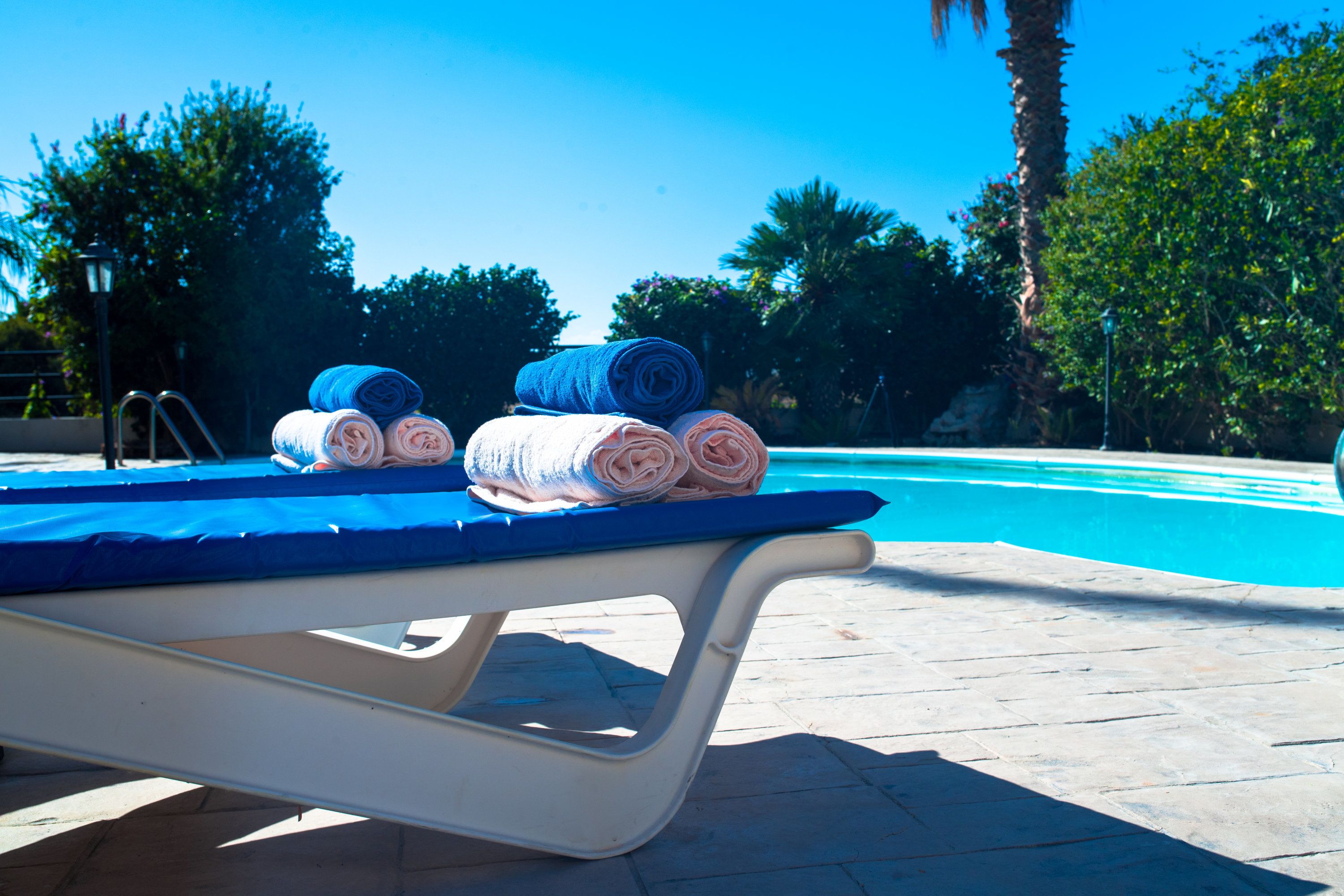Un salon au bord de la piscine, avec un fauteuil bleu rembourré et des serviettes enroulées.