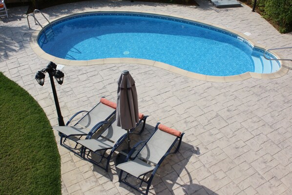 Una piscina de borde curvo, rodeada por un patio empedrado con sillas de descanso y una sombrilla.