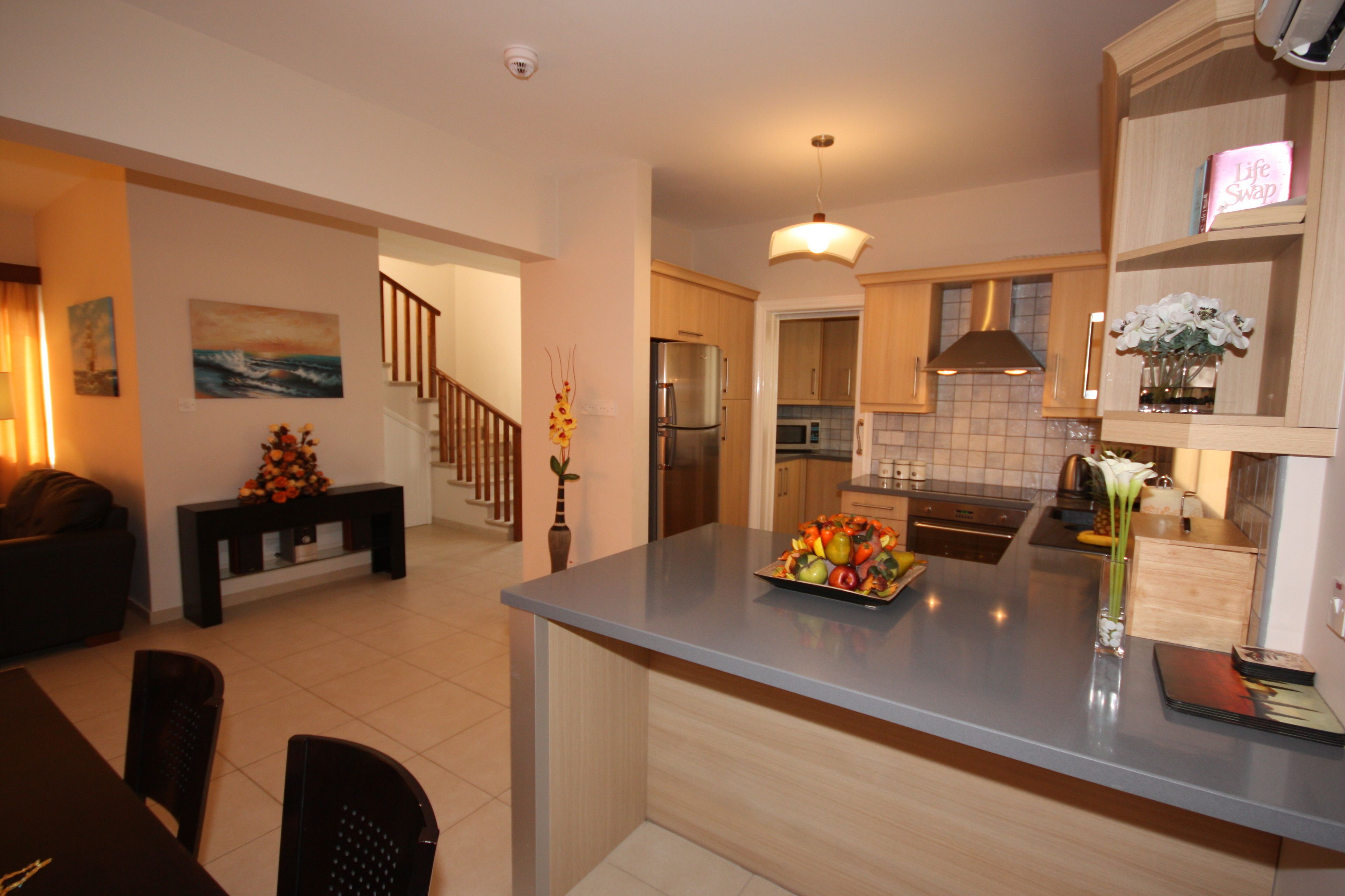 Una cocina moderna con una isla central, armarios de madera y un comedor con una mesa y sillas de madera oscura.