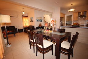 A dining area with a glass-top table, wooden chairs, and a centerpiece of fruit and flowers. - Vineland Bay Villas (Pissouri)