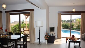 A spacious living room with a dining area, a flat-screen TV, and a view of a swimming pool.