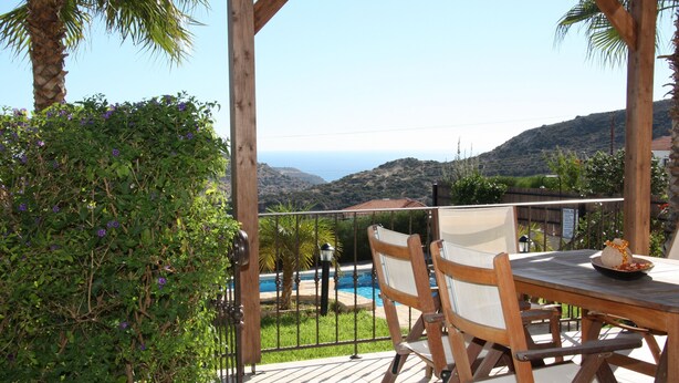 Una mesa de madera con sillas, vista a una piscina y un paisaje montañoso.