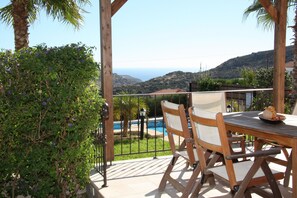 Mesa de madeira com cadeiras, vista para uma piscina e paisagem montanhosa.