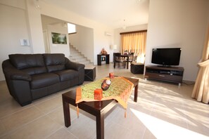 A living room with a dark leather sofa, a wooden coffee table, a flat-screen TV, and a staircase leading to another level.